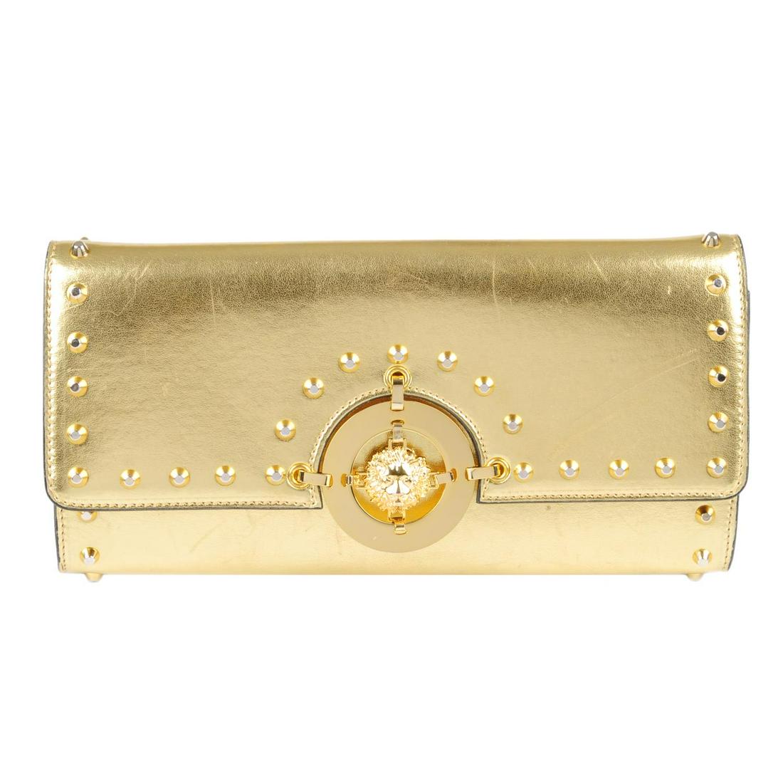 VERSUS BY VERSACE - a gold leather clutch. Crafted from: VERSUS BY VERSACE - a gold leather clutch. Crafted from metallic gold leather, with gold-tone studded trim and lion medallion to the centre, hidden magnetic snap fastening, optional chain strap and li