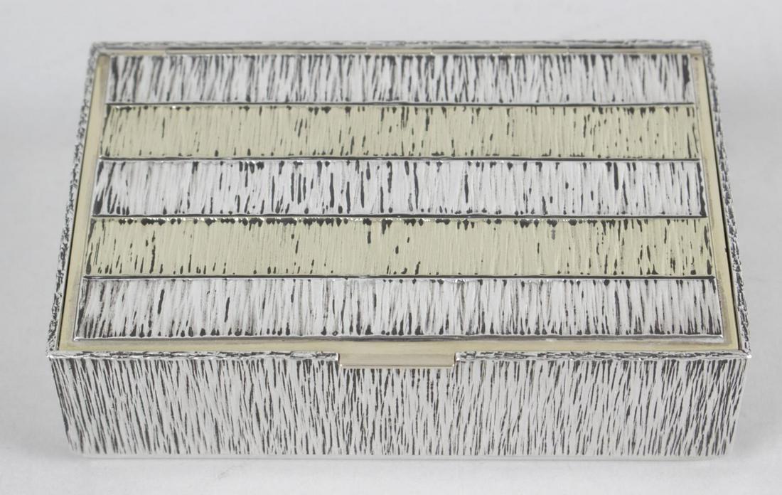 A 1970's silver box by Gerald Benney, the rectangular: A 1970's silver box by Gerald Benney, the rectangular form with textured and bark-effect surface detail to the whole and hinged lid with alternating silver and gilt panels, opening to a leather lined