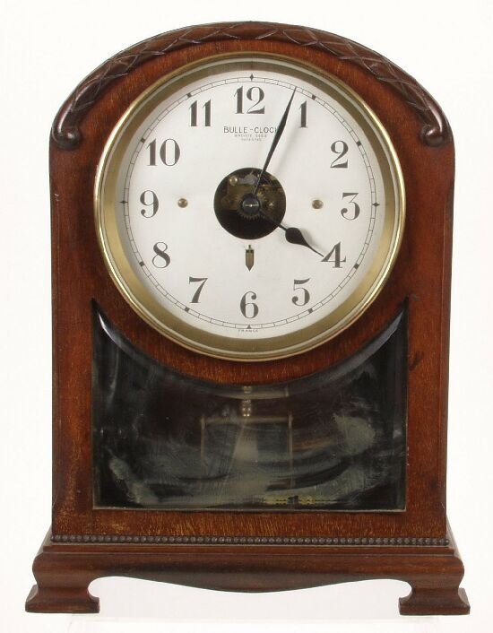 A Bulle electric mantel clock, the mahog: A Bulle electric mantel clock, the mahogany and boxwood strung arched case with glazed panel displaying the pendulum, the white painted dial with Arabic numerals and brass bezel, on brass compressed b