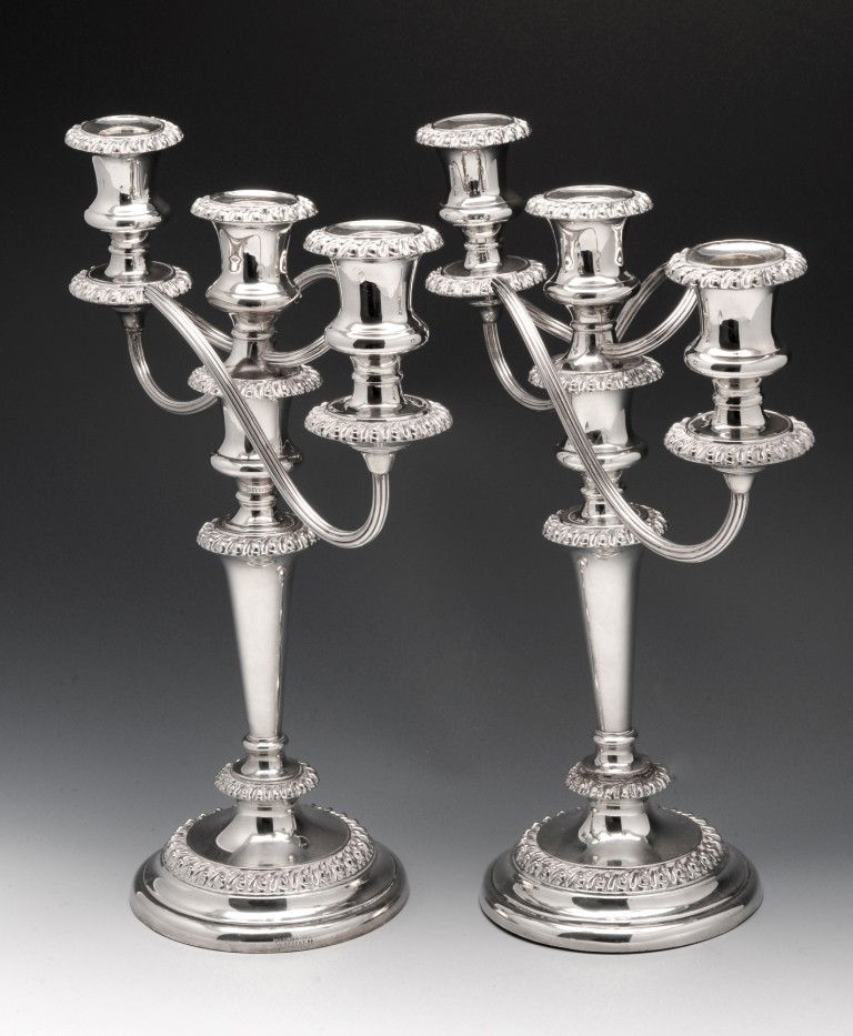 A pair of silver plated candelabra.: A pair of silver plated candelabra each raised above a circular stepped base with shaped tapered columns and gadrooned borders, twin reeded and scrolling branches and three sockets with detachable noz