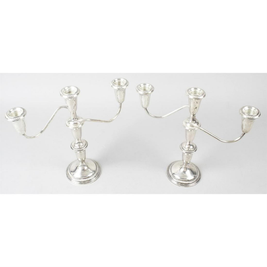 A pair of sterling silver twin-branch candelabra: A pair of sterling silver twin-branch candelabra, each with circular base rising to a vase shape stem with removable upper sections and looped branches leading to conforming vase shape sockets, with r