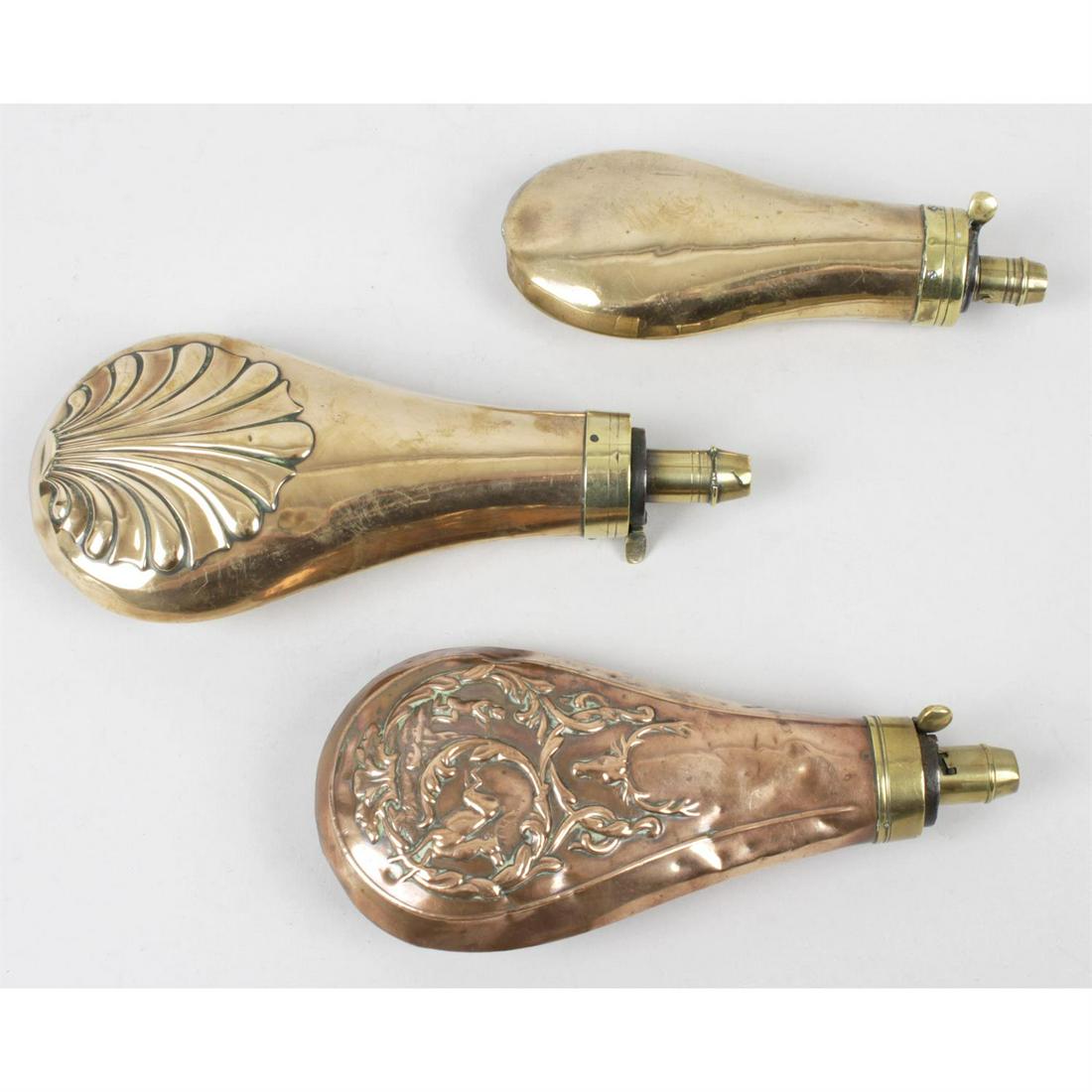 Three late 19th century copper and brass powder/shot flasks.: Three late nineteenth century copper and brass powder/shot flasks, one with raised decoration depicting a shell, height 8" (20.25cm), one with raised decoration depicting a hunting scene, height 7.25"