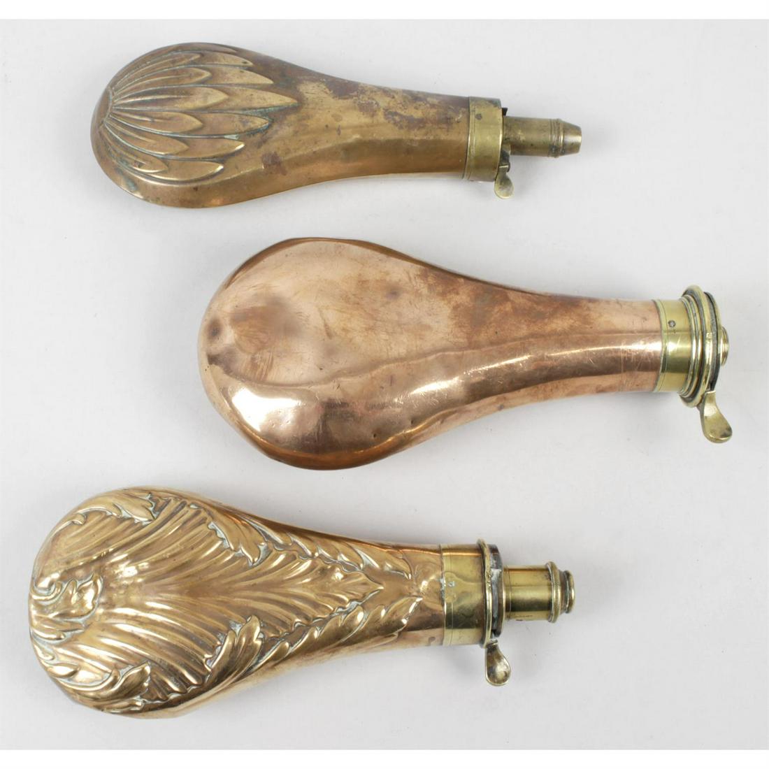 Three late 19th century copper and brass powder/shot flasks.: Three late nineteenth century copper and brass powder/shot flasks, one with raised decoration depicting birds, height 7.5" (19cm), one with raised decoration depicting flower petals, height 8" (20cm),