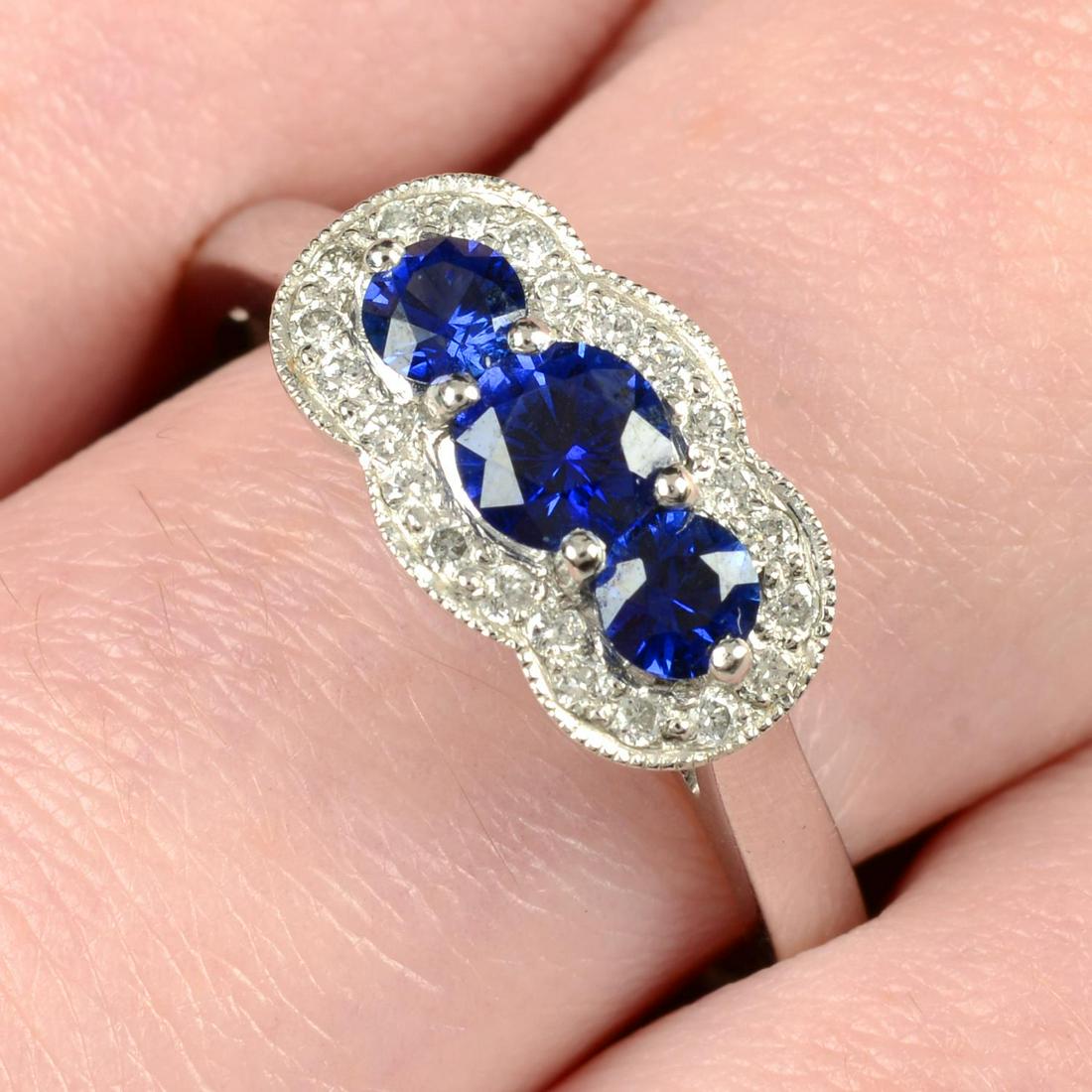 A platinum graduated sapphire three-stone ring, with brilliant-cut diamond shared surround.Sapphire (1 of 5)