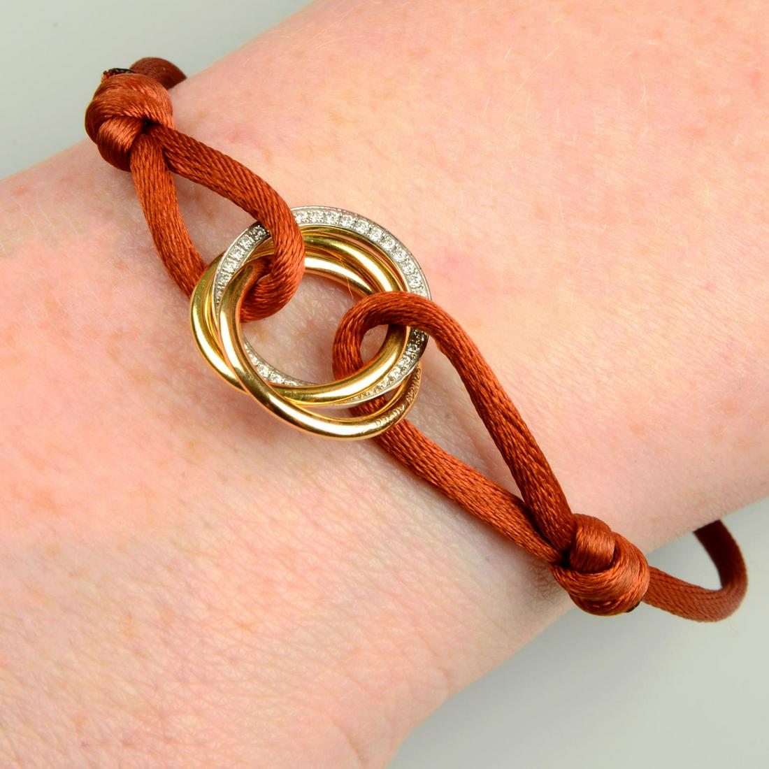 An 18ct gold brilliant-cut diamond 'Trinity' bracelet, on adjustable brown cord, by Cartier.Total (1 of 3)