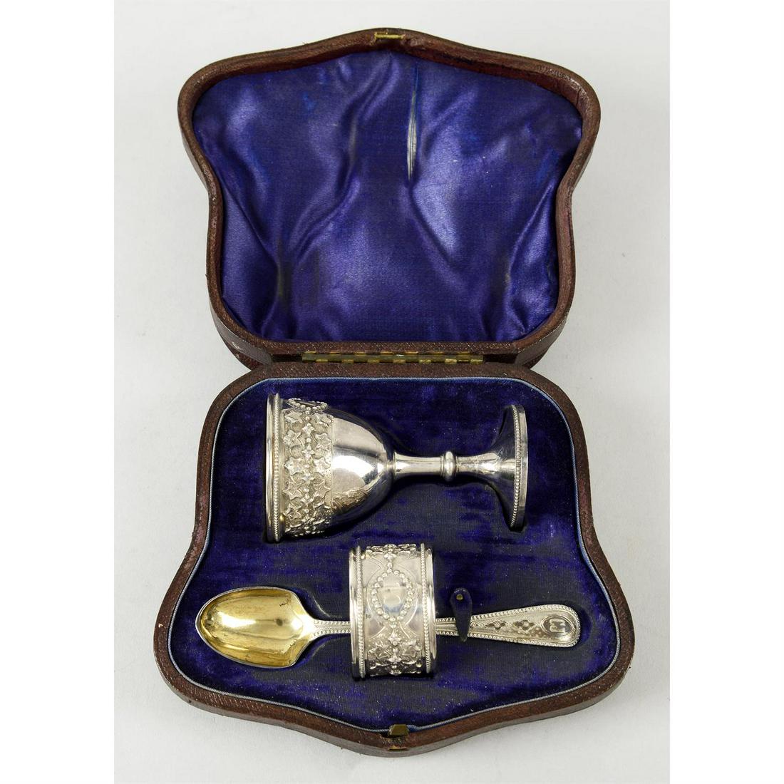 A mid-Victorian silver cased christening set.: A mid-Victorian silver cased christening set, comprising egg cup, spoon and napkin ring, each item having decorative embossing or engraving surrounding central, initial engraved cartouche. Hallmarked