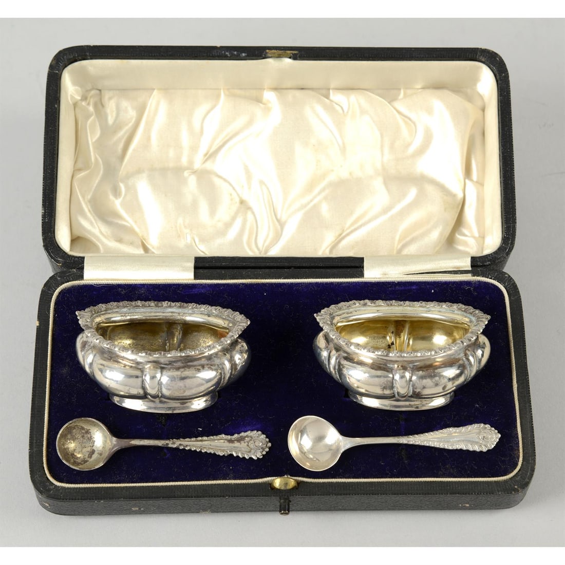A cased pair of George V silver open salts.: A cased pair of George V silver open salts, of squat, lobed form with frilled rims, hallmarked Walker & Hall, Sheffield 1913, together with two condiment spoons with plumed edge, hallmarked A Chick &
