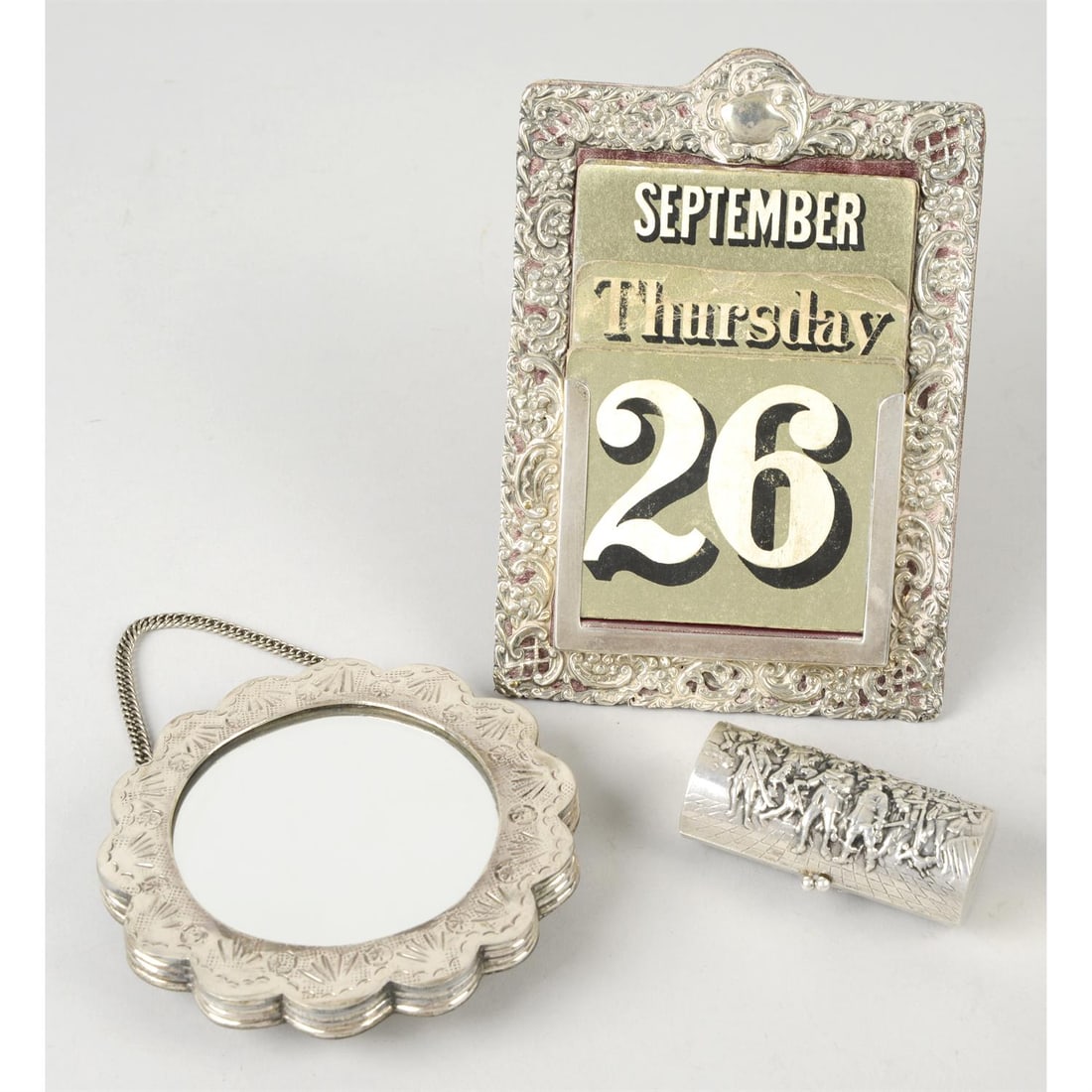 A silver mounted desk calendar; plus a small mirror on chain marked 900 & a cylindrical purse: A silver mounted desk calendar, having pierced, scrolled and cross-hatched design, hallmarked Chester 1899, plus a small, flower shaped and embossed mirror on chain, marked 900, and a cylindrical purs