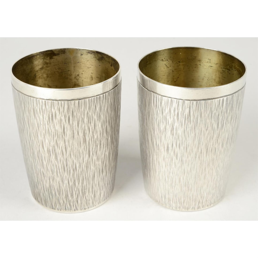 Pair of Gerald Benney silver tumbler cups.: A pair of Gerald Benney silver tumbler cups, having bark effect texture below plain rims and personalised engraving to bases. Hallmarked London 1975. Height 9cm, overall weight 11.4ozt (354.5g). Condi