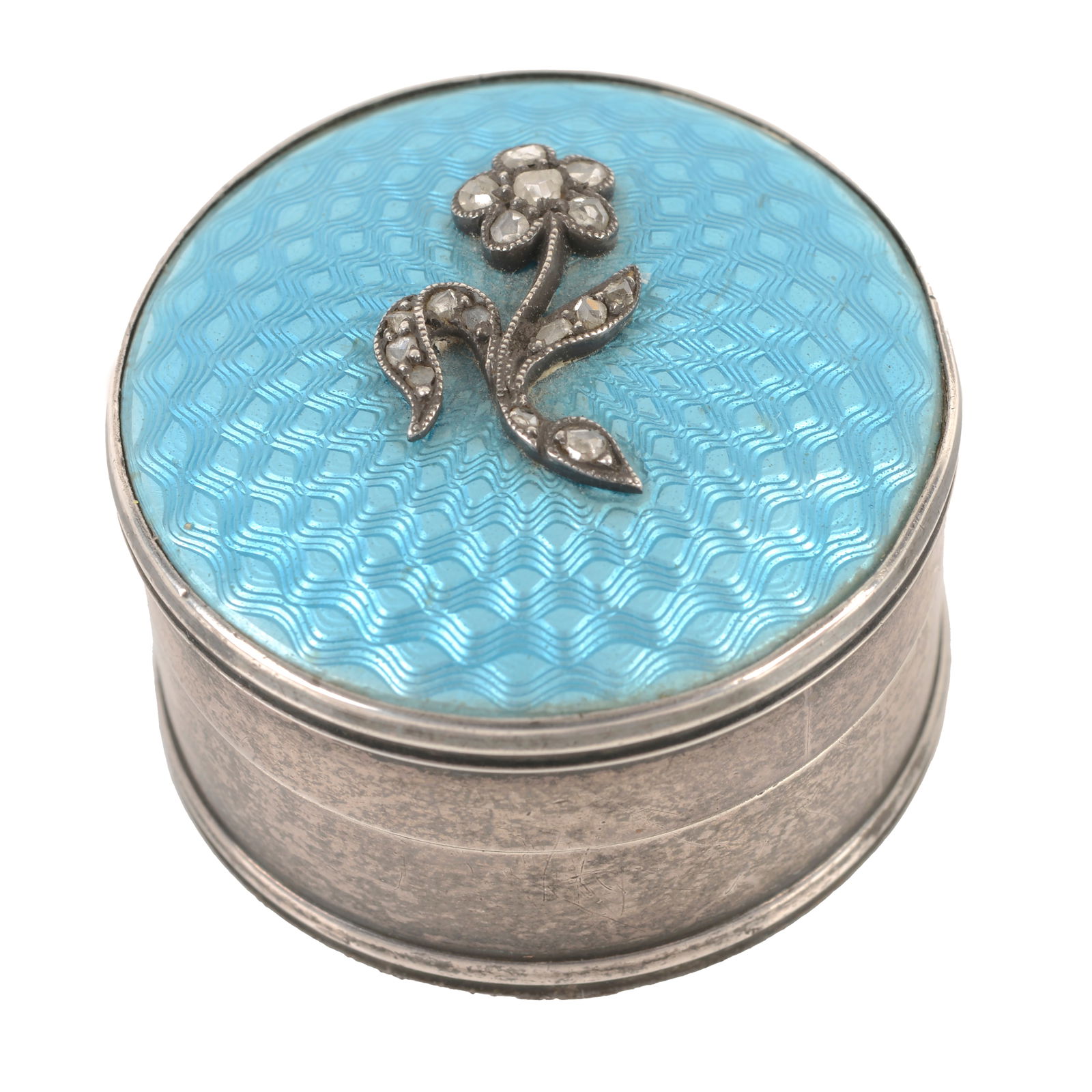 Silver and enamel diamond set pill box: Silver and enamel diamond set pill box A George V silver and enamel circular pill box, the hinged lid decorated in sky blue guilloché enamel with applied rose cut diamond forget-me-not to the c