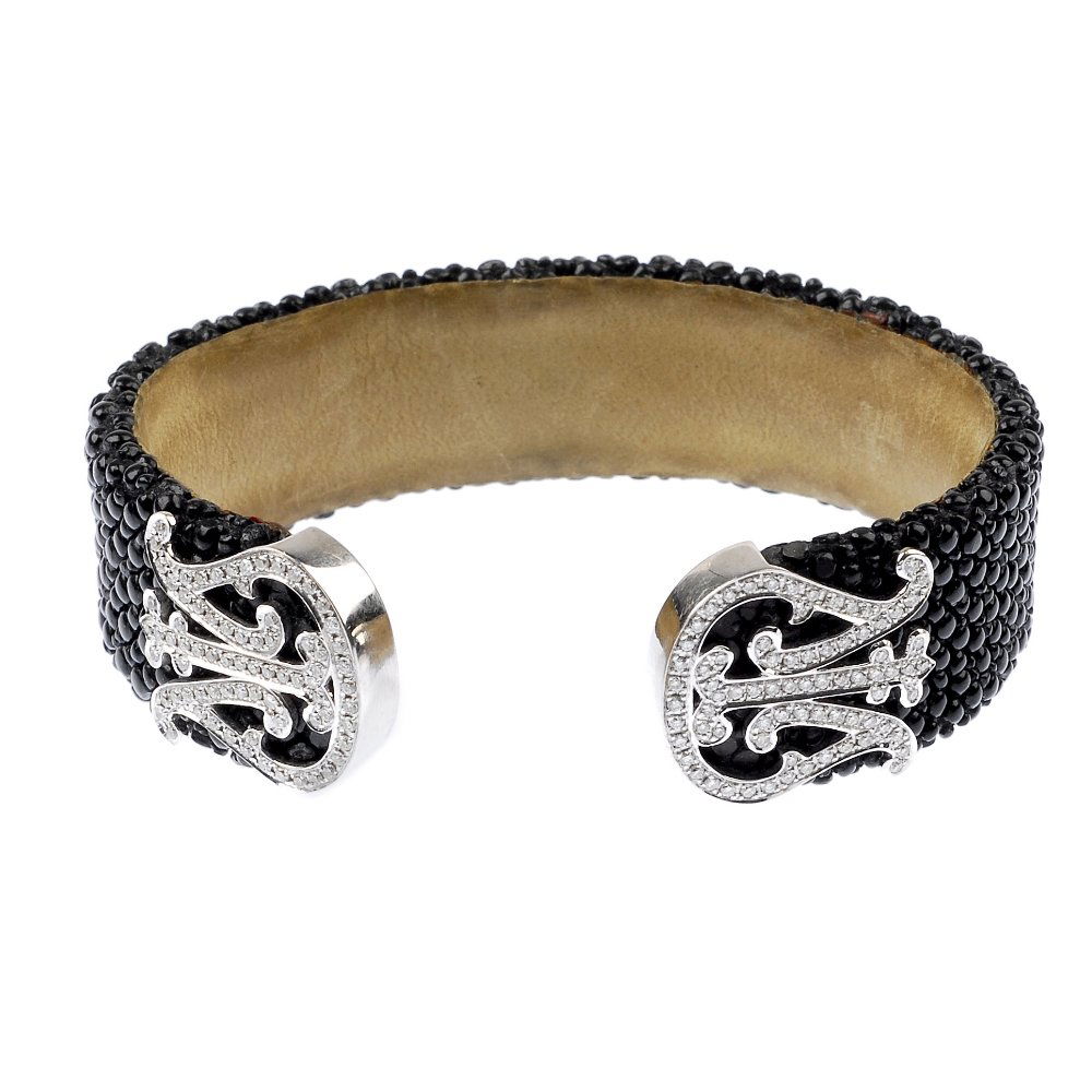 (529489-2-A) TECHNOMARINE - A diamond cuff.: (529489-2-A) TECHNOMARINE - a diamond cuff. Designed as a textured black cuff, with brilliant-cut diamond lyre terminals. Signed Technomarine. Estimated total diamond weight 0.90ct. Inner diameter 5.8