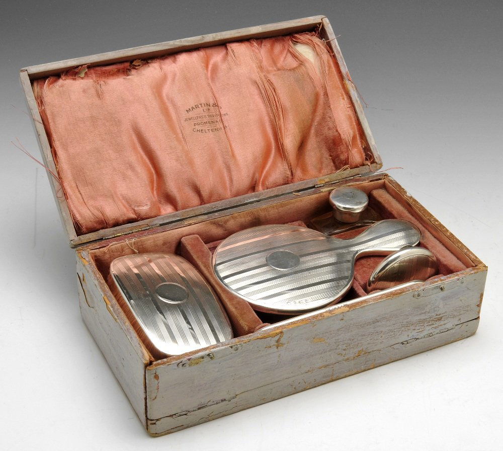 An early 20th century silver mounted travelling dressin: An early twentieth century silver mounted travelling dressing table set, comprising a hand mirror, pill box, brush, scent bottle and plastic comb, with engine-turned geometric motif, cased. Hallmarked