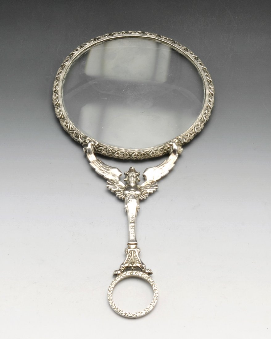 An early 20th century French silver magnifying glass.: An early twentieth century French silver magnifying glass, the glass within a pierced, stylised foliate mount, to the winged caryatid handle and carrying loop. French assay marks to loop. Length 7 3/4