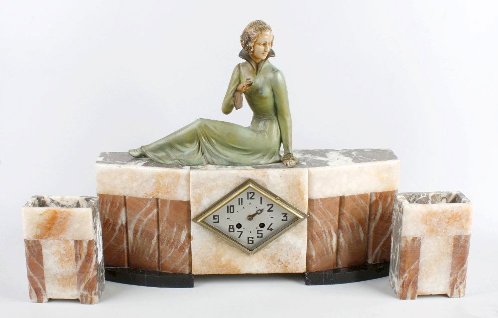An Art Deco-style three-piece marble clock garniture: An Art Deco-style three-piece marble clock garnitureThe clock surmounted by a spelter reclining female figure over lozenge-shaped Arabic dial, 17" (43cm) high, together with a pair of oblong vases, (3