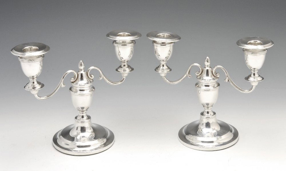 An Edwardian pair of small silver twin branch candelabr: An Edwardian pair of small silver twin branch candelabra with urn shaped stems, reeded borders and central flame terminal, loaded. Hallmarked London 1906, the maker possibly Goldsmiths & Silversmiths