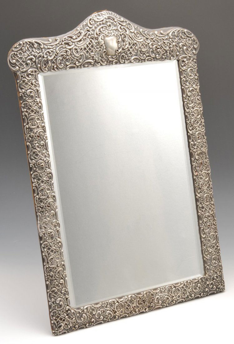 A late Victorian silver mounted dressing table mirror.: A late Victorian silver mounted dressing table mirror, the oblong form with applied silver in floral scroll open-work relief, bevelled edge mirror and easel back. Hallmarked Henry Matthews, Birmingham