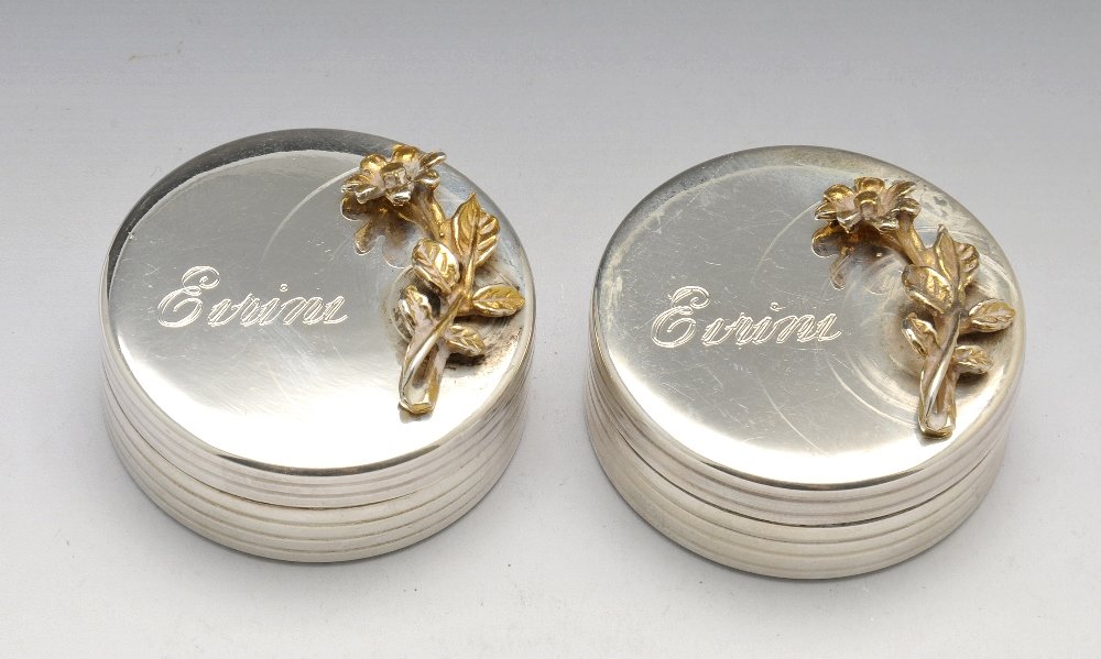 A collection of eleven pill/trinket/bonbonniere boxes.: A pair of circular form trinket boxes, each of plain outline with ribbed edge and decorated with an applied floral sprig to the removable lid alongside a personal name engraving, impressed '925' to th