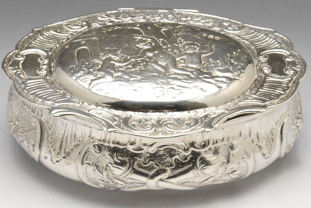 A Victorian import silver table snuff or tobacco box.: A Victorian import silver table snuff or tobacco box, the oval hinged form decorated with a putti scene amongst floral scrolls and panels of torches and bow and arrows. Hallmarked Martin Sugar, London