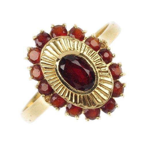 A garnet cluster ring.: A garnet cluster ring. The oval-shape garnet collet, within a radial surround, to the circular-shape garnet border and plain band. Weight 4.4gms.