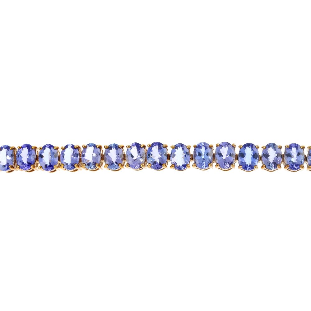 A 9ct gold tanzanite line bracelet.: A 9ct gold tanzanite line bracelet. Designed as a series of oval-shape tanzanite, to the partially concealed clasp. Hallmarks for Birmingham. Length 19.2cms. Weight 21.5gms.