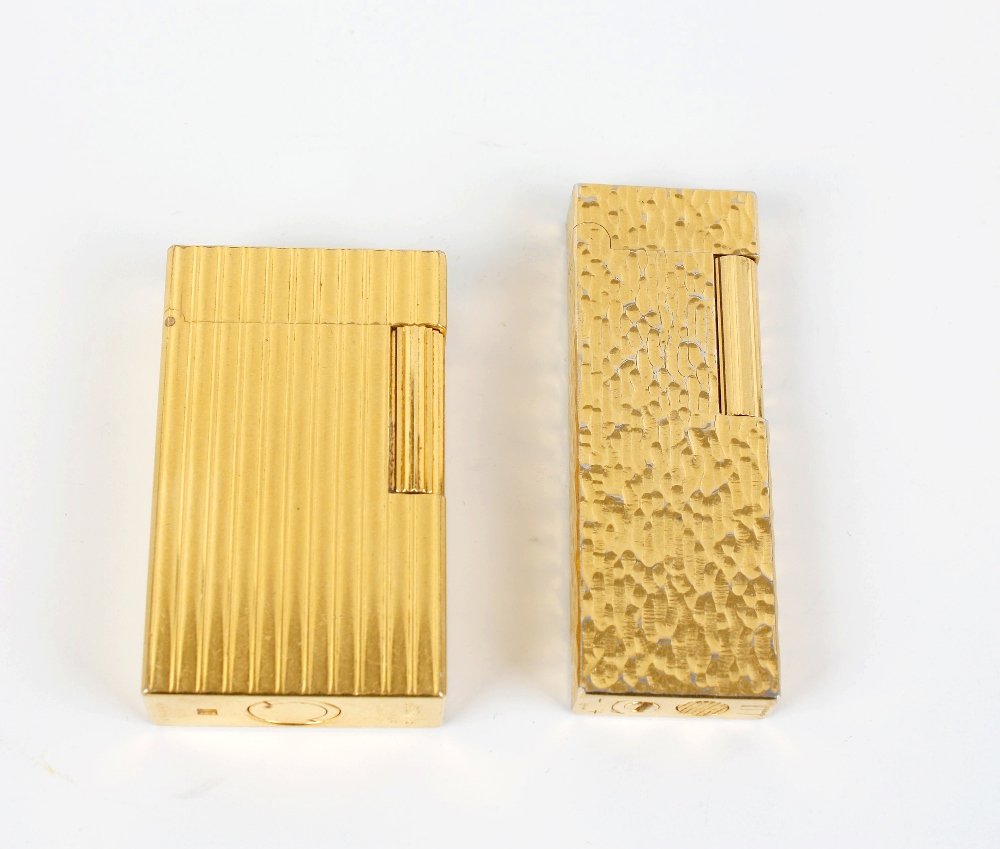 Two gold plated cigarette lighters: Two gold plated cigarette lighters, the first with textured bark effect finish, stamped Dunhill Japan, 2.75" (7cm) high. The second with ribbed decoration, stamped ST Dupont Paris, Made in France, 10G