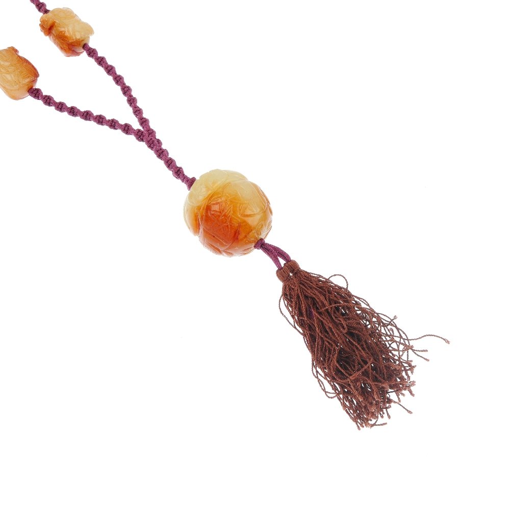 Two carved green gem bead necklaces.: Two carved green gem bead necklaces, each designed as a carved green and brown gem bead, suspending a fabric tassel, to the woven fabric back-chain with carved gem bead spacers. Length 46cms.