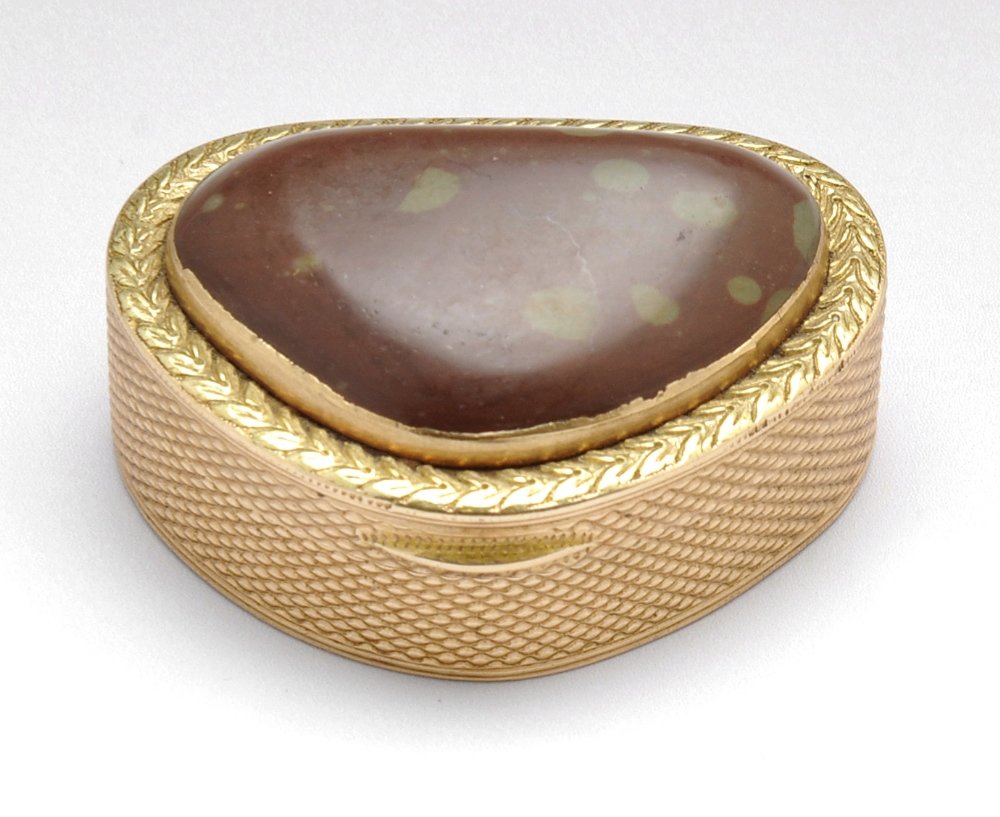 A nineteenth century gold coloured vinaigrette.: A nineteenth century gold coloured vinaigrette, the rounded triangular form with engine turned decoration to the hardstone set lid with foliate border opening to the simple pierced grille. Engraved to