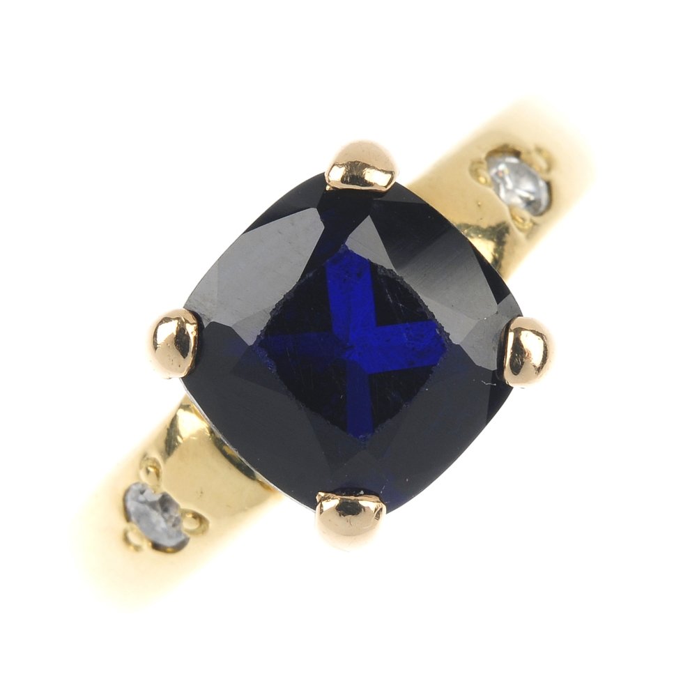 An 18ct gold synthetic sapphire and paste ring.: An 18ct gold synthetic sapphire and paste ring. The square-shape synthetic sapphire to the circular-shape colourless paste sides and tapered band. Hallmarks rubbed. Weight 9.6gms.