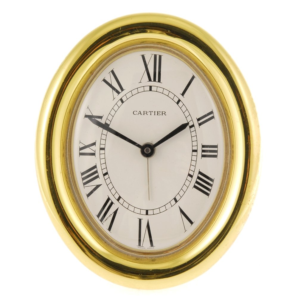 (124060) A gold plated quartz travel alarm clock by: (124060) A gold plated quartz travel alarm clock by Cartier, the cream dial with hourly applied black Roman numeral markers, the oval case, numbered 890813384, fitted with a signed movement. Case widt