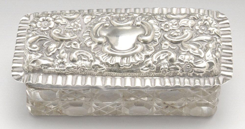 An Edwardian silver mounted glass vanity box.: An Edwardian silver mounted glass vanity box of oblong form, the silver lid with floral scroll embossing and crimped rim. Hallmarked William Aitken, Birmingham 1904. Length measuring 3 1/4 inches (8.5
