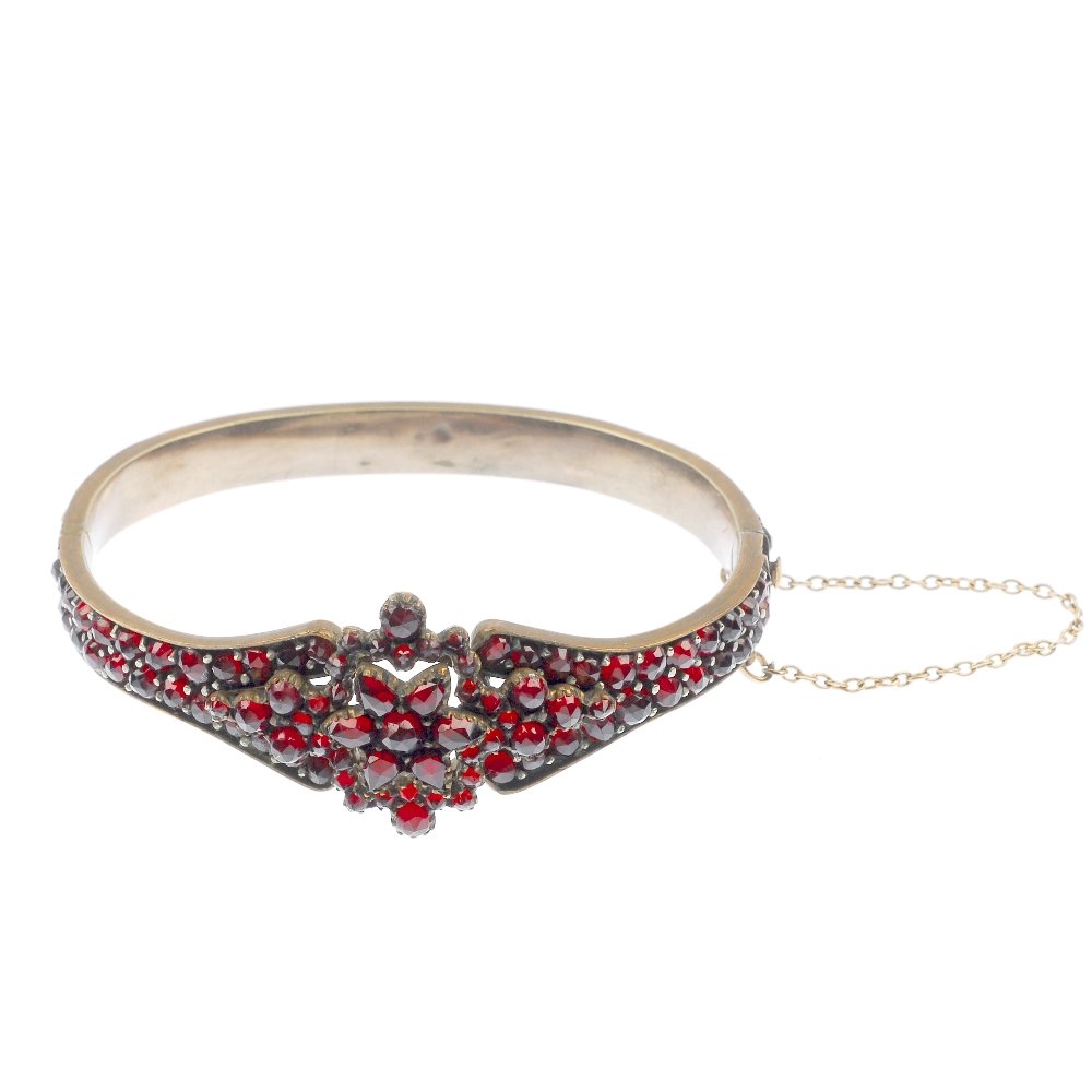A late 19th century garnet and paste bangle.: A late 19th century garnet and paste bangle, the circular and pear-shape cluster star, to the similarly-set surround and hinged band, set throughout with multi-faceted garnet and red paste. Inner diam