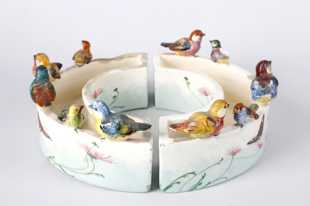 A French Delphine Massier (Vallauris) pottery posy ring: A French Delphine Massier (Vallauris) pottery posy ring, formed as two semi circles, each surmounted by perching birds, over painted flowers and butterflies, 11" (28cm) diameter, (A/F).