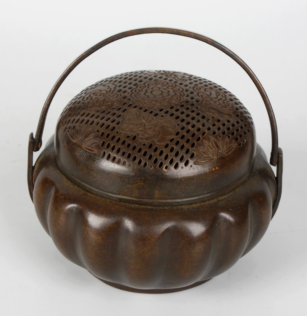 A Chinese bronze incense burner or hand-warmer: A Chinese bronze incense burner or hand-warmer, the domed pierced circular cover beneath swing handle, the squat reeded pumpkin form body with Archaistic style seal mark beneath, 3.5" diameter x 2.5" 