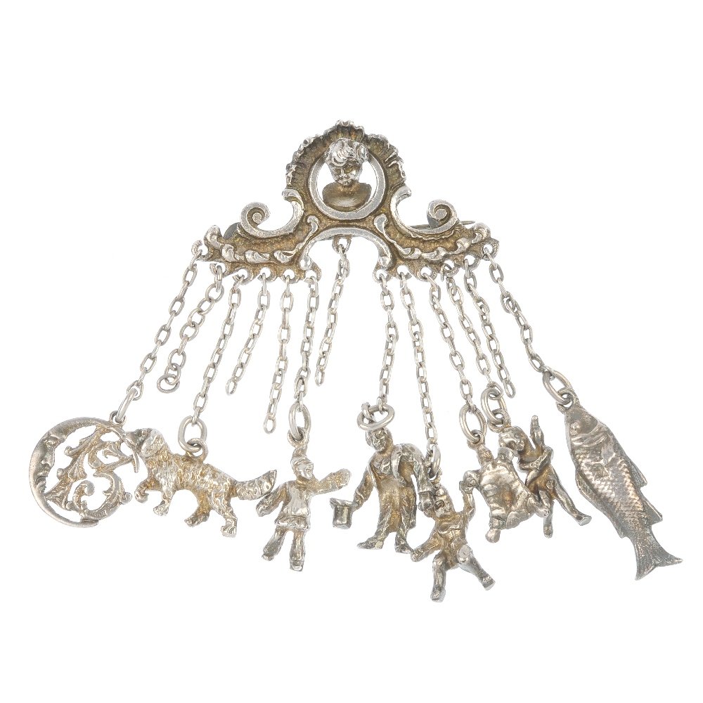 A late 19th century silver charm brooch: A late 19th century silver charm brooch, designed as a series of eight charms, to include a fish and a dog, suspended from a scrolling shell surmount with bust centre. Five charms deficient. Length 8.