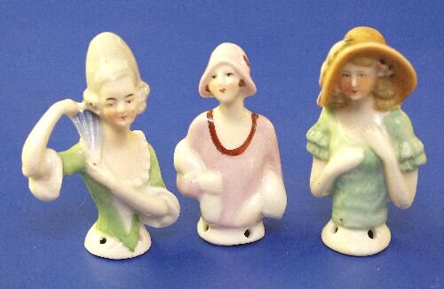 Three porcelain half dolls, one modelled: Three porcelain half dolls, one modelled as a lady in a 1920's style hat, fur wrap and coat, another of a lady holding aloft a fan, and the other of a lady wearing a feather decorated hat.
