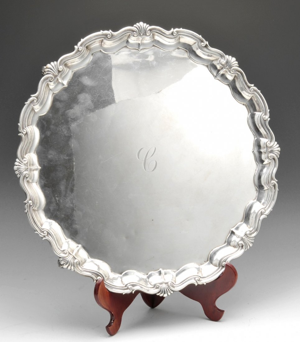 An early twentieth century large silver salver.: An early twentieth century large silver salver, the circular form with central initial engraving, raised edge with shell and scroll rim, standing on three scroll feet, small personal inscription to th