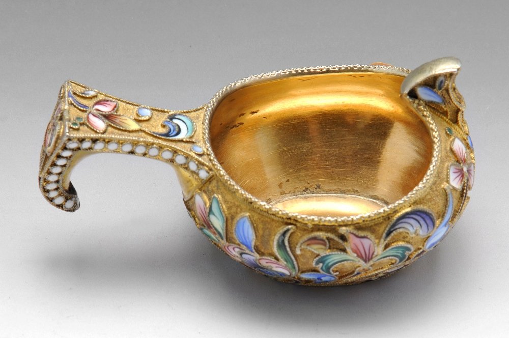 An early 20th century Russian silver-gilt and cloisonne: An early twentieth century Russian silver-gilt and cloisonné enamel kovsh, the stylised floral enamel in shades of blue, purple, pink and green, the handle bordered by white beading and all upon a si