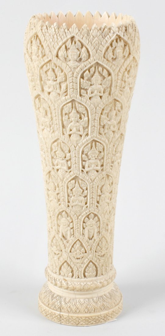 A South East Asian ivory vase: A South East Asian ivory vase, late 19th century, of tapering cylindrical form with serrated rim, the whole carved with tiers of arcaded motifs, each row with various depictions of Buddhist figures an