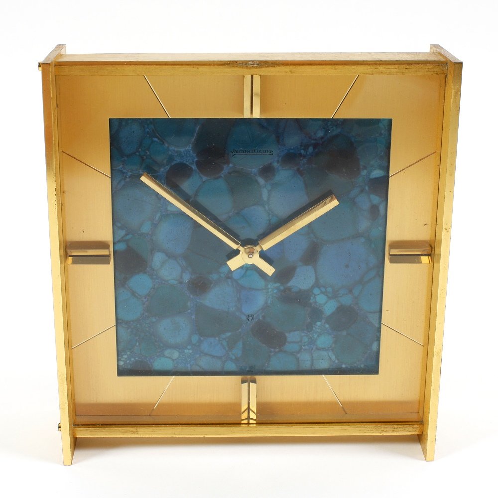A Jaeger LeCoultre brass-cased mantel clock: A Jaeger LeCoultre brass-cased mantel clock, circa 1970, with square dial, baton quarters and hands framing a mottled turquoise-effect cellular field, with back-wound movement, the simple brushed case