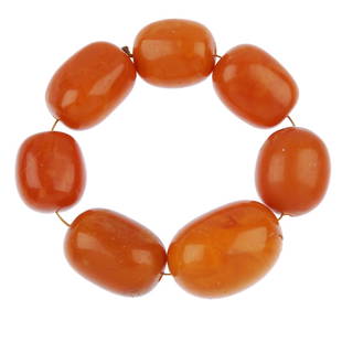 A string of seven natural amber beads.: A string of seven natural amber beads, in the form of a bracelet, the barrel-shape beads measure 27 to 38mm. Length 30cms. Weight 80gms.