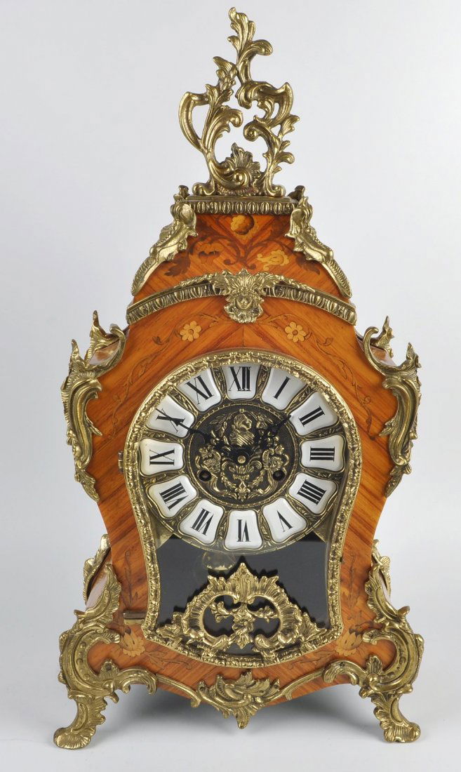A modern marquetry mantel clock: A modern marquetry mantel clock. With cellular Roman dial, German two-train movement striking on two bells, the flower-inlaid waisted case with gilt metal mounts, 22.75", (58cm) high.