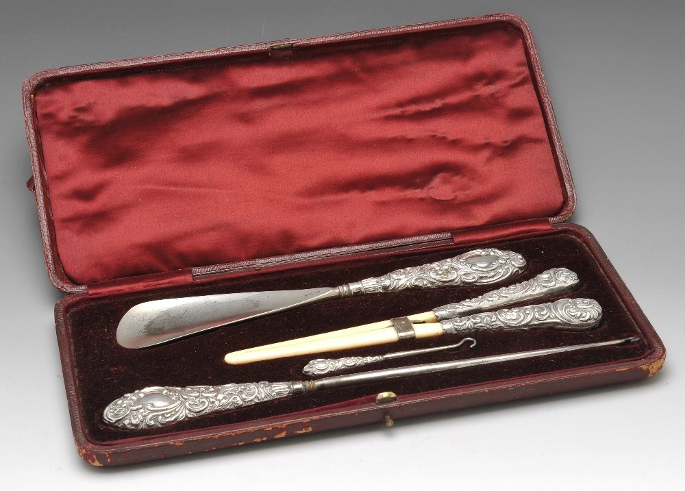 A late Victorian cased and silver mounted shoe horn and: A late Victorian cased shoe horn and button set, to include a pair of ivory glove stretchers, a shoe horn and button and shoe hooks, each with scrolling foliate filled silver handles. Hallmarked Henry
