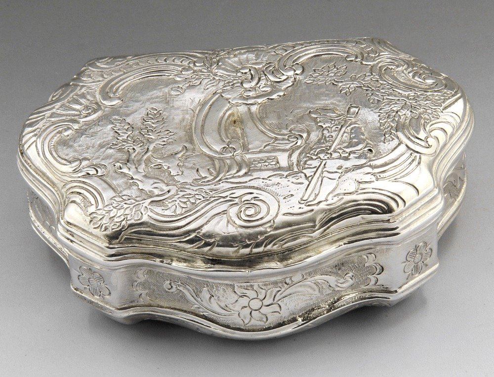 A twentieth century snuff box of shaped form.: A twentieth century silver import snuff box, of shaped form, the hinged lid with pastoral scene, to the scalloped shell and scrolling sides and base. Import marks for BCT Co Ltd., London 1924. Length 