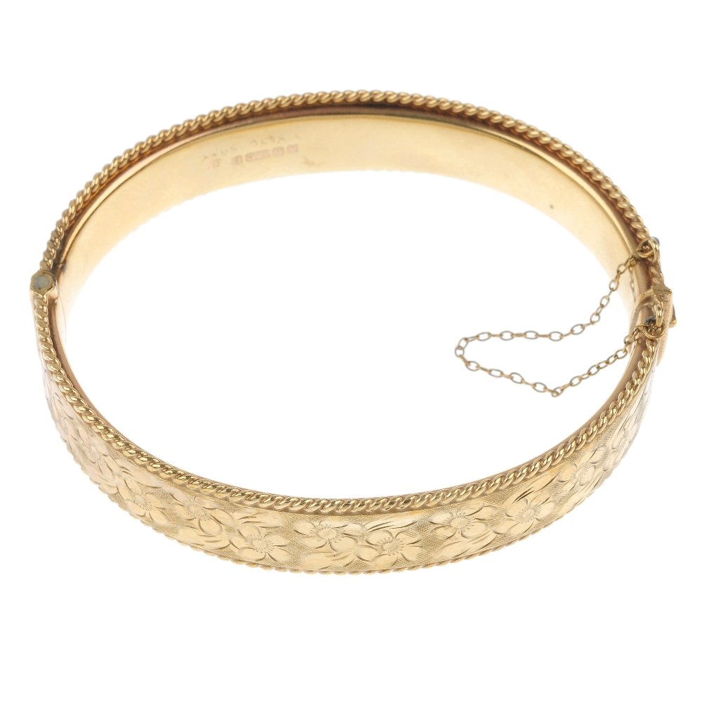 A 9ct gold hinged bangle.: A 9ct gold hinged bangle. The front designed as a floral embossed panel with rope-twist sides, to the similarly-designed half-bangle. Hallmarks for Birmingham, 1970. Inner diameter 6.3cms. Weight 21gm