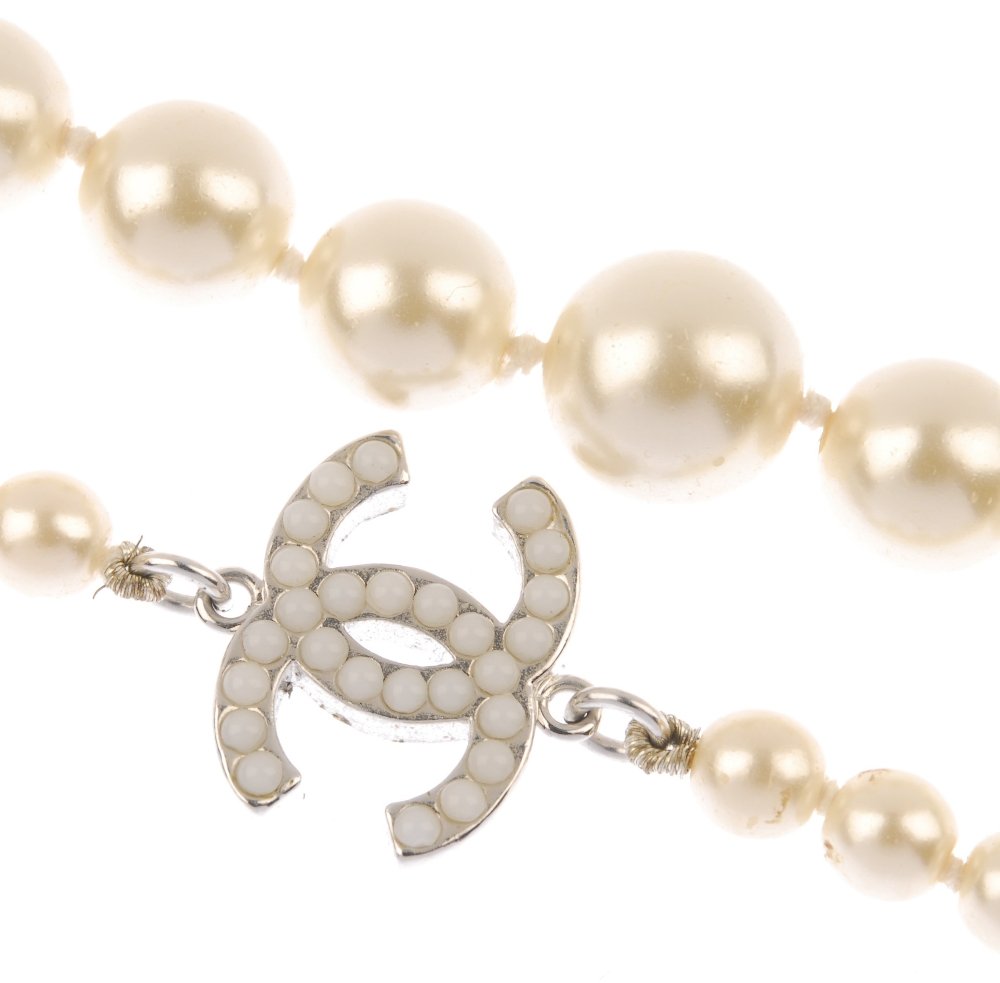 (2350-4-A) CHANEL - an imitation pearl single-strand ne: (2350-4-A) CHANEL - an imitation pearl single-strand necklace. Designed as a single row of imitation pearls, with Chanel logo accents. Signed Chanel. Length 95cms. With maker's case and pouch.