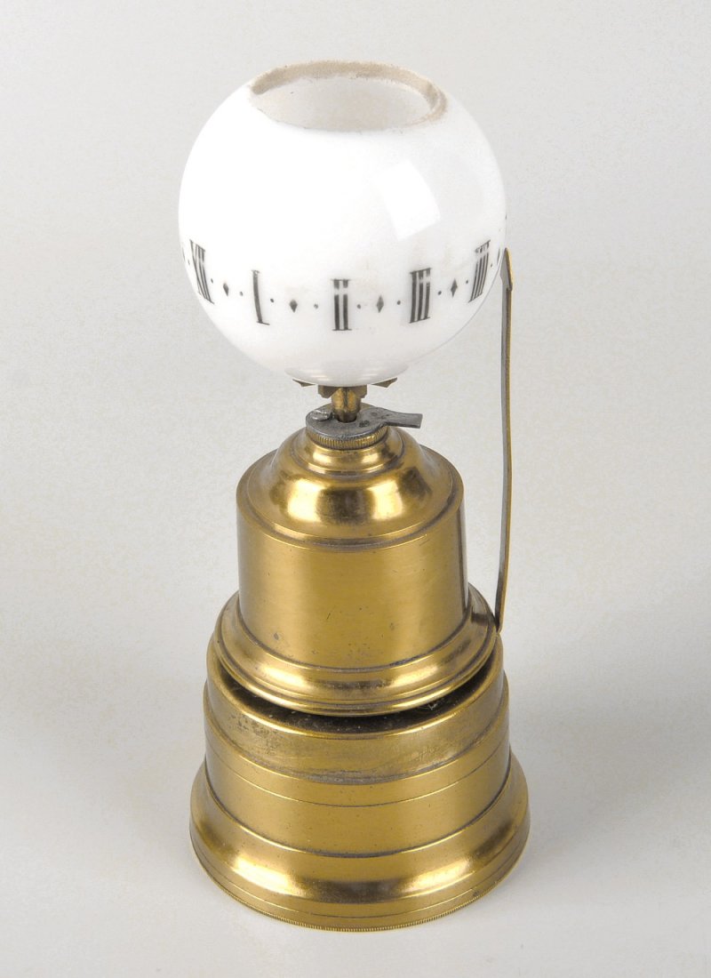 An early 20th century night lamp clock: An early 20th century night lamp clock, with rotating opaque glass dome having Roman numerals, raised upon a brass pedestal base with vertical indicator and timepiece movement, 4.75" (12cm) high, with