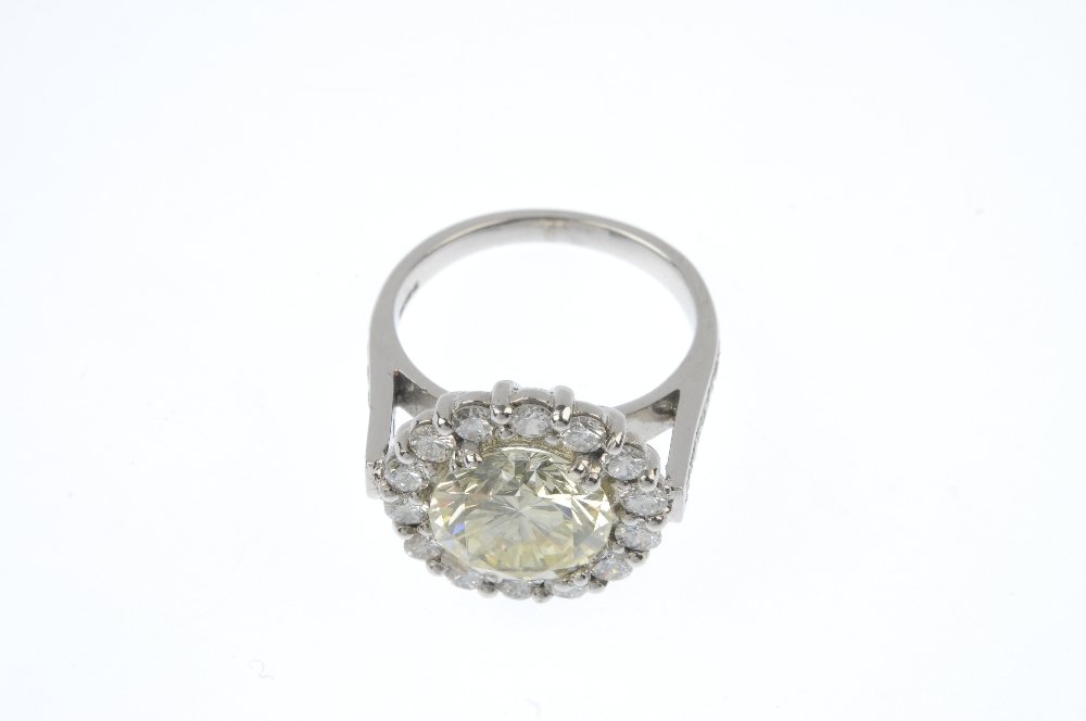 An 18ct gold 'Fancy Light Yellow' diamond and diamond: An 18ct gold coloured diamond and diamond cluster ring. The brilliant-cut Fancy Light Yellow diamond, weighing 4.08cts, within a brilliant-cut diamond surround, to the pave-set diamond shoulders and p
