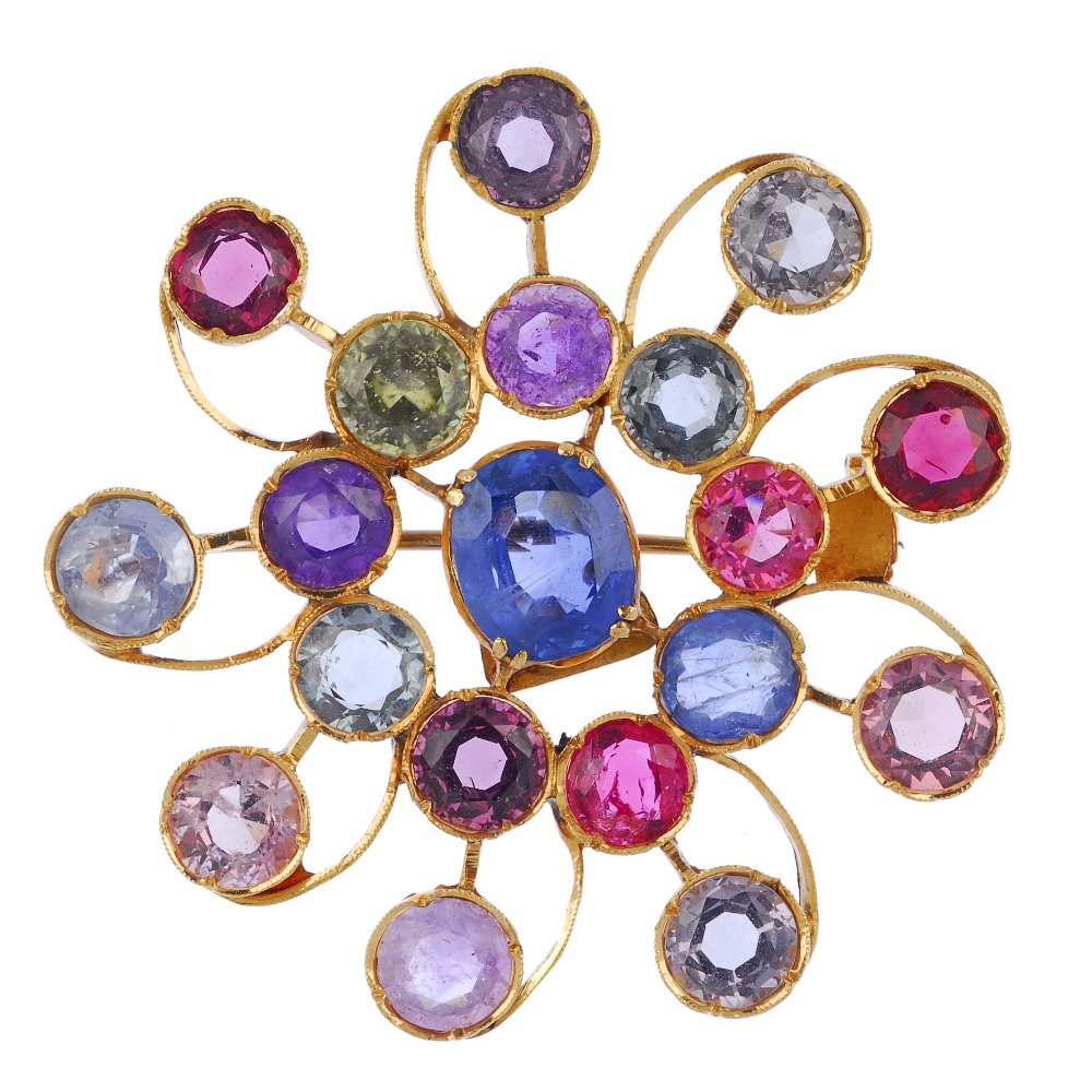 A multi-gem brooch.: A multi-gem brooch. Of openwork design, the oval-shape blue sapphire, within a circular-shape multi-gem surround, to include vari-shade sapphire and zircon, to the similarly-set scrolling border. Diam