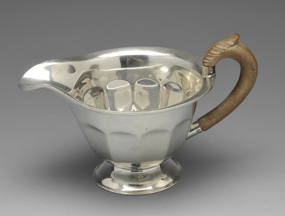 A 1930's silver cream jug.: A 1930's silver cream jug, the circular facetted form standing on a circular foot and with wooden handle. Hallmarked Sir John Bennett Ltd, London 1935. Height measuring 3 1/2 inches (9 cm), weight 4.3