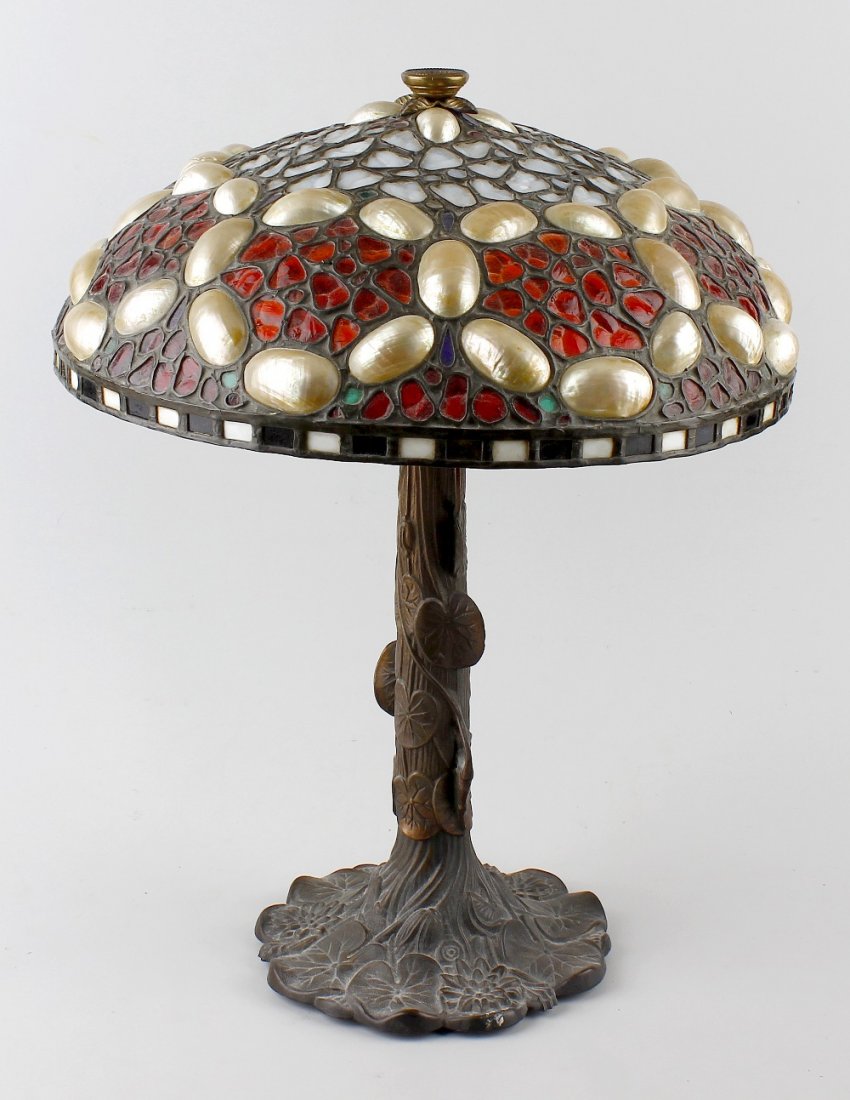 An Art Nouveau table lamp.: An Art Nouveau table lamp, the domed and lead-glazed shade inset with pearlescent shells and coloured glass panels, the bronzed cast metal base modelled as a tree with trailing vines, 16.5" (45.5 cm)